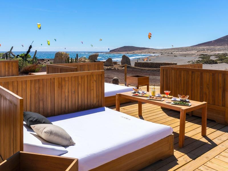 Bains de soleil en bois confortables sur terrasse avec vue sur la mer et cerfs-volants colorés.