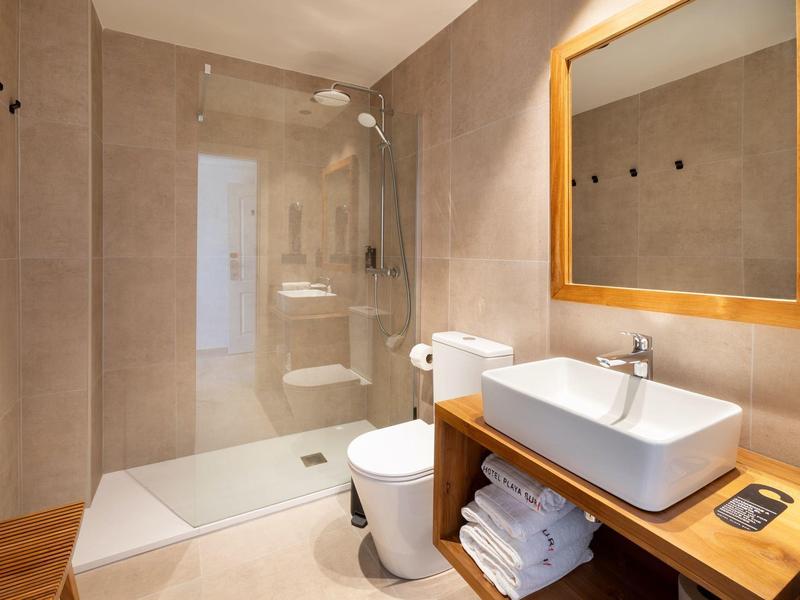 Salle de bain moderne avec douche à l'italienne, toilettes et lavabo avec étagère en bois et miroir.
