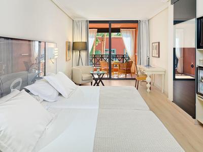 Lichte hotelkamer met twee bedden, balkon met zitplaatsen en modern interieur.