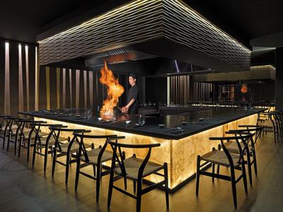 Modern restaurant met centrale grill en zwarte inrichting onder gedimd licht.