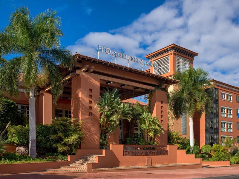 Hotel met tropische gevelbegroeiing, palmbomen en een zonnige lucht.