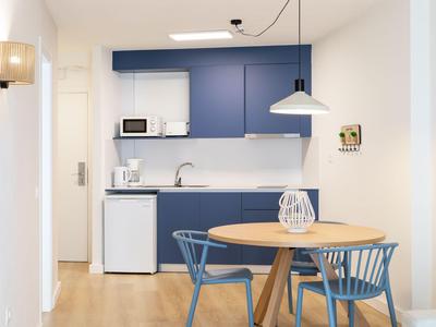 Kleine Hotelküche mit blauem Schrank, runder Holztisch und blauen Stühlen.