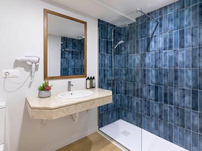 Modernes Badezimmer mit blauen Kacheln, begehbarer Dusche und Waschtisch mit Spiegel.