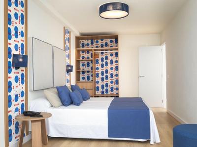 Modernes Hotelzimmer mit blau-weißem Design, großem Bett und offenem Kleiderschrank.