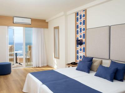 Modernes Hotelzimmer mit Balkon und Meerblick, weißen Wänden und blauer Bettwäsche.