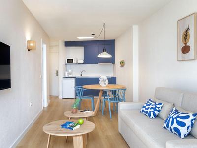 Helles Hotelzimmer mit Sofa, Esstisch, Küchenzeile und modernem Dekor in Blau und Weiß.