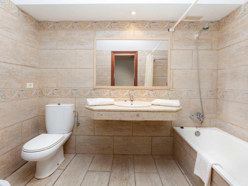 Baño luminoso con inodoro, lavabo doble, espejo de pared y bañera con ducha.