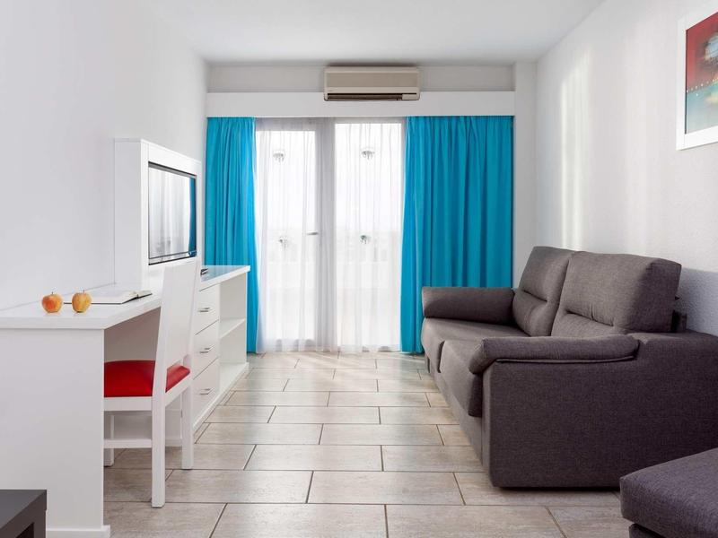 Sala de estar moderna con sofá gris, escritorio blanco y cortinas azules junto a ventanales