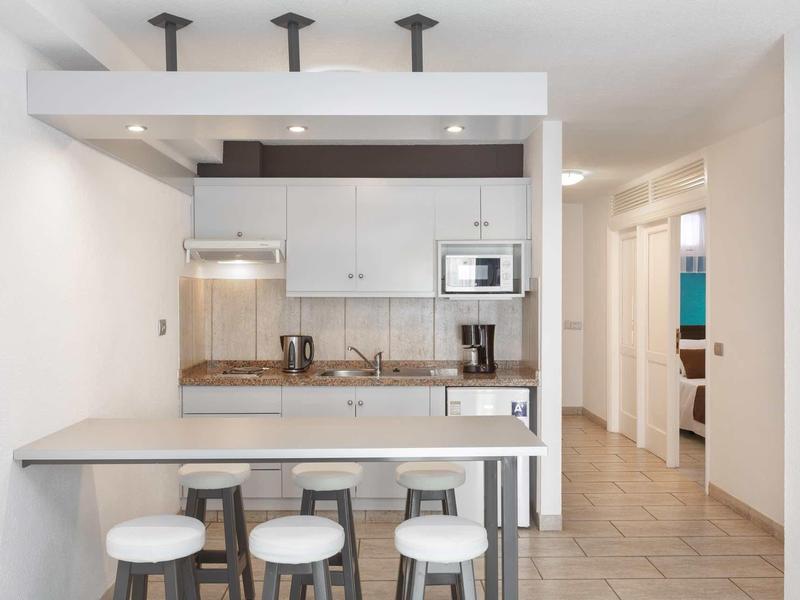 Cocina moderna con taburetes, cafetera y microondas en espacio abierto y luminoso.