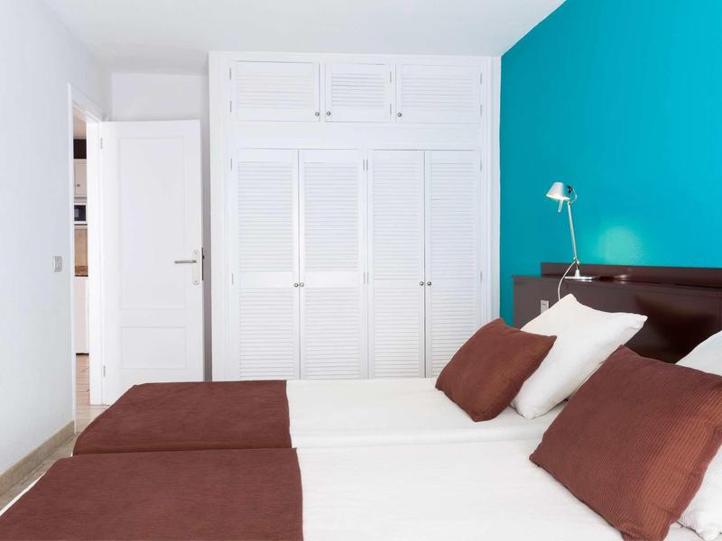 Dormitorio con dos camas, paredes blancas, pared de acento turquesa y armario empotrado blanco.