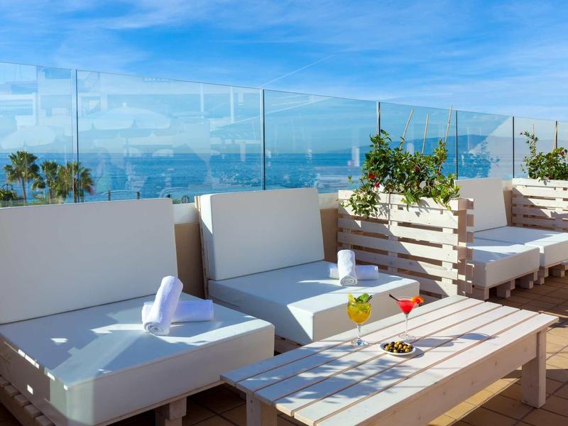 Terraza en la azotea con conjunto de asientos blancos modernos, protección de vidrio y vista al mar en el horizonte.