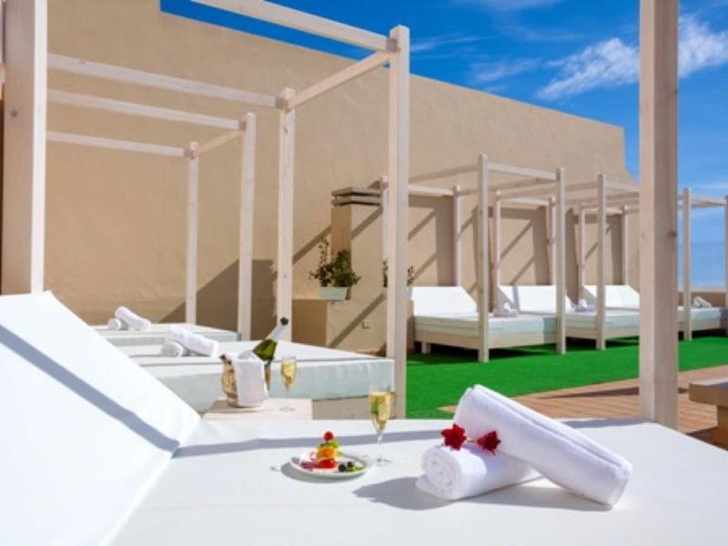 Terraza de hotel con tumbonas blancas, toallas dobladas y aperitivos bajo un cielo azul