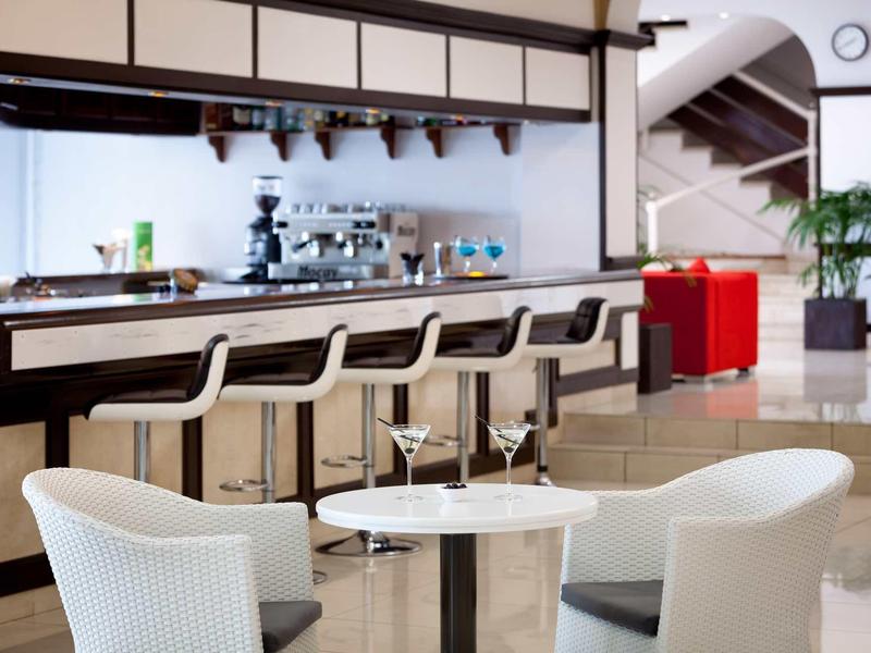 Área moderna de salón de hotel con barra, taburetes y asientos en un espacio luminoso y abierto.