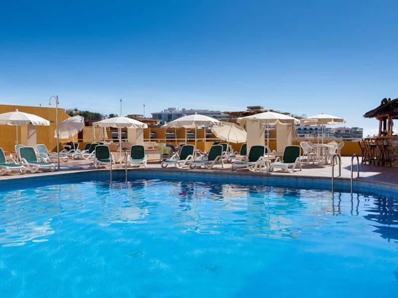 Gran piscina de hotel con tumbonas y sombrillas bajo un cielo azul claro.