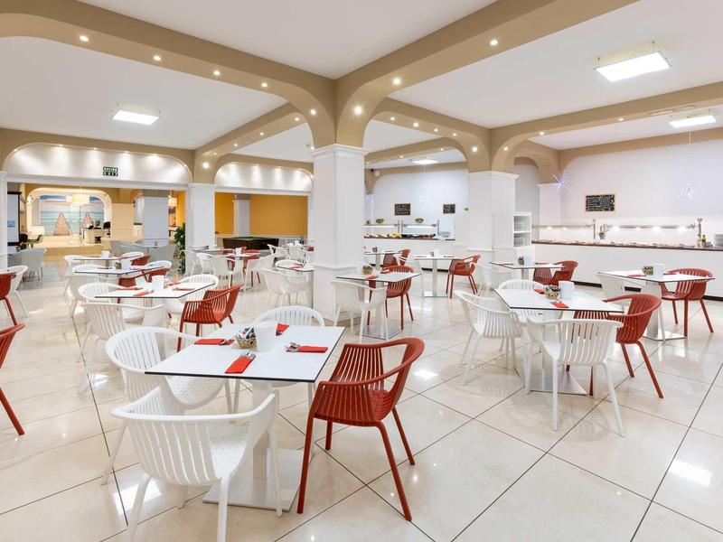 Comedor moderno y luminoso con sillas blancas y rojas y mesas cuadradas.