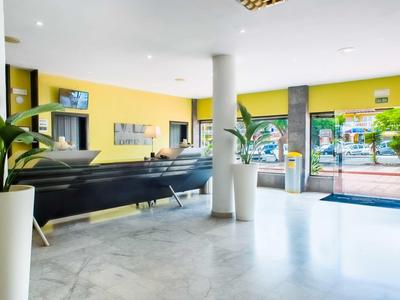 Luminoso atrio d'hotel con pareti gialle, divani neri e grandi finestre di vetro.