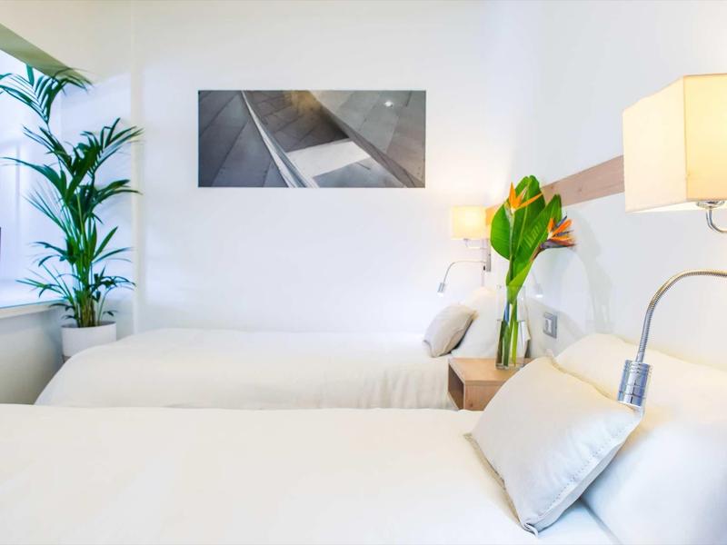 Bright hotel room with two beds, decorations, and natural light from a window.