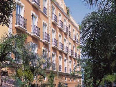 Vícepodlažní hotelová budova s balkony, obklopená palmami a modrou oblohou.