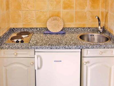 Kleine Küchenzeile mit grauer Arbeitsplatte, weißem Mini-Kühlschrank, Herd und Spüle.