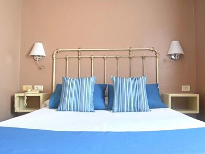 Schlichtes Schlafzimmer mit weißem Bett, blau-weiß gestreiften Kissen und beige Wänden.