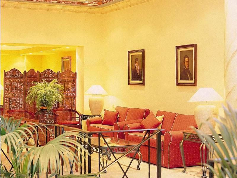 Helles Wohnzimmer mit rotem Sofa, zwei Lampen, grünen Pflanzen und zwei gerahmten Bildern an der Wand.