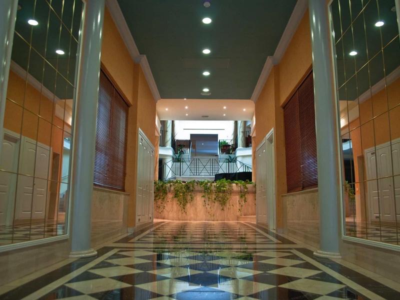 Flur mit schwarzem-weißem Musterboden, weißen Wänden und Deckenspots führt nach draußen.