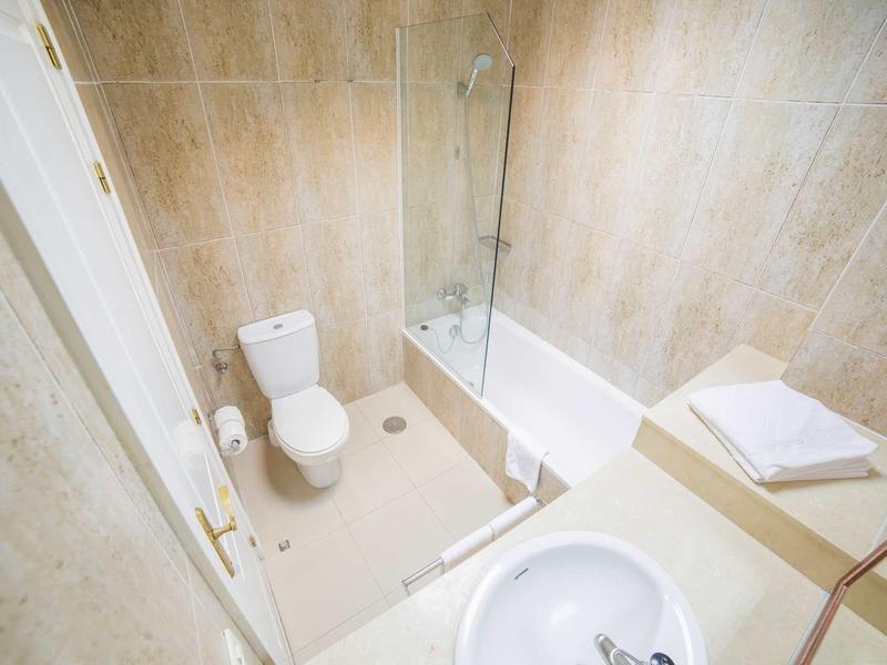 Kleines Badezimmer mit Toilette, Badewanne, Waschbecken und beiger Wand- und Bodenfliesen.