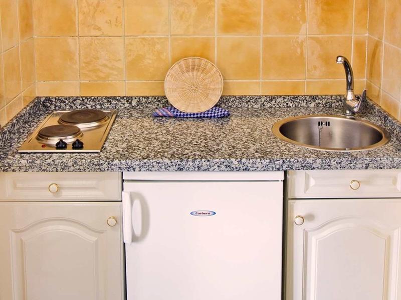 Kleine Küchenzeile mit grauer Arbeitsplatte, weißem Mini-Kühlschrank, Herd und Spüle.