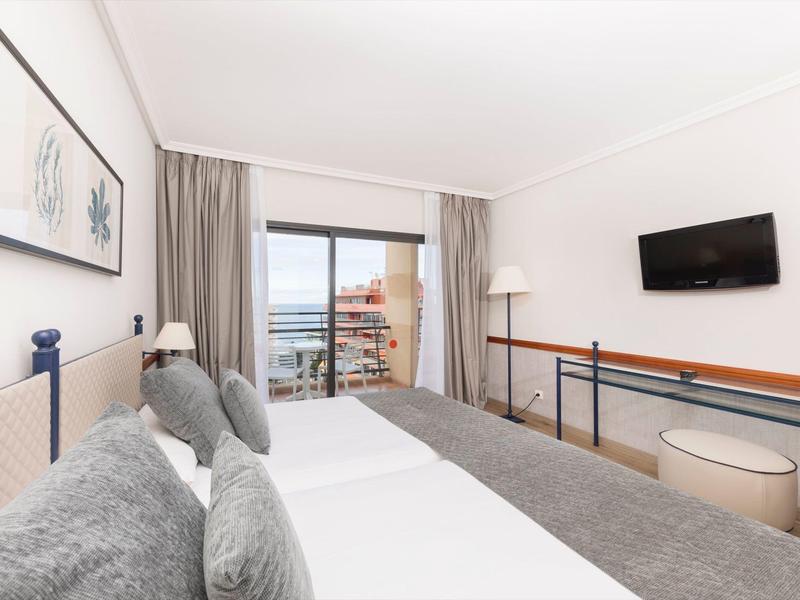 Camera d'hotel moderna con due letti singoli, TV e vista mare dal balcone