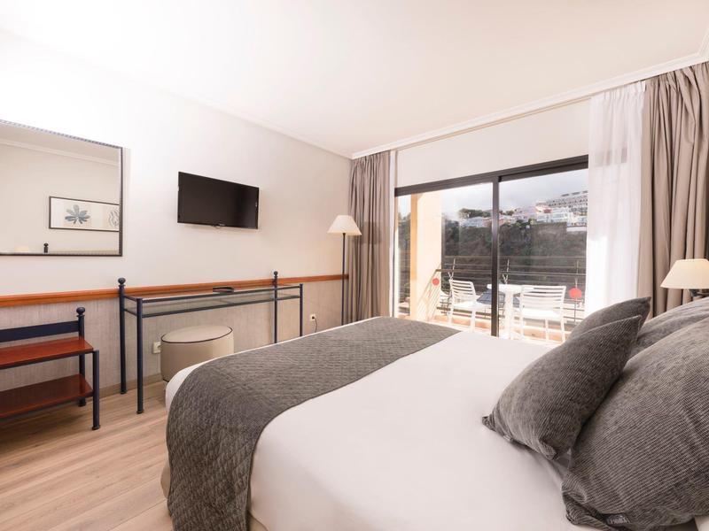 Camera d'hotel moderna con letto grande, scrivania, sedia e accesso a un balcone.