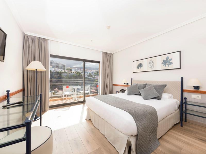 Camera d'hotel luminosa con letto matrimoniale, arredamento moderno e terrazza con vista esterna.