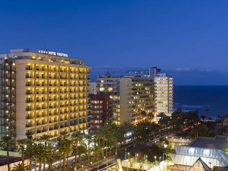 Edificio dell'hotel con balconi illuminati di notte, palme e mare sullo sfondo