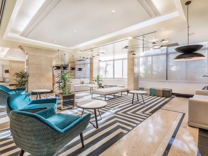 Luminoso e moderno atrio d'hotel con poltrone blu, divani e tappeto geometrico.