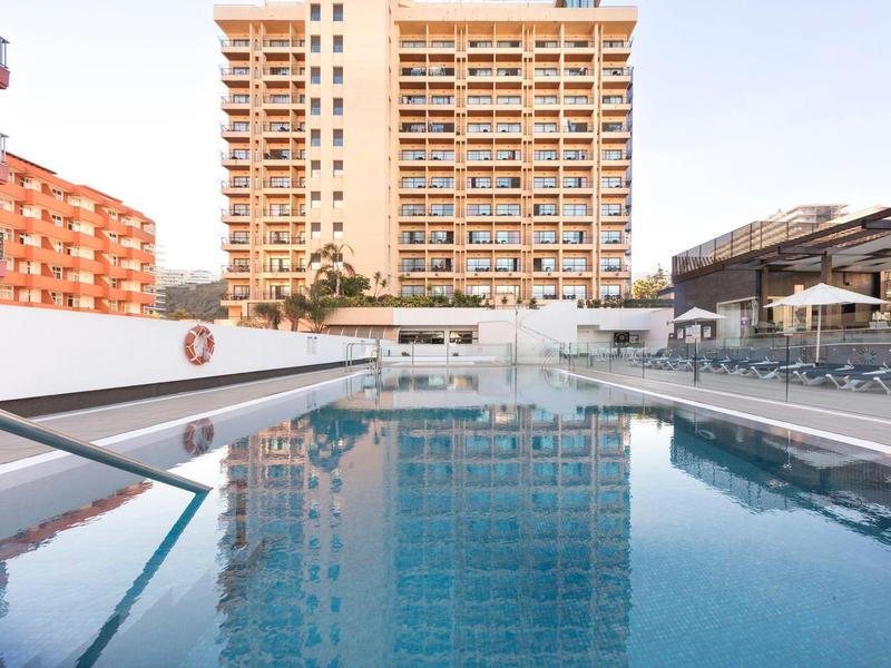 Piscina all'aperto moderna con lettini e un alto edificio residenziale sullo sfondo.