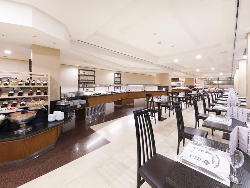 Spazio ristorante luminoso con buffet seduto e tavoli apparecchiati in design moderno.