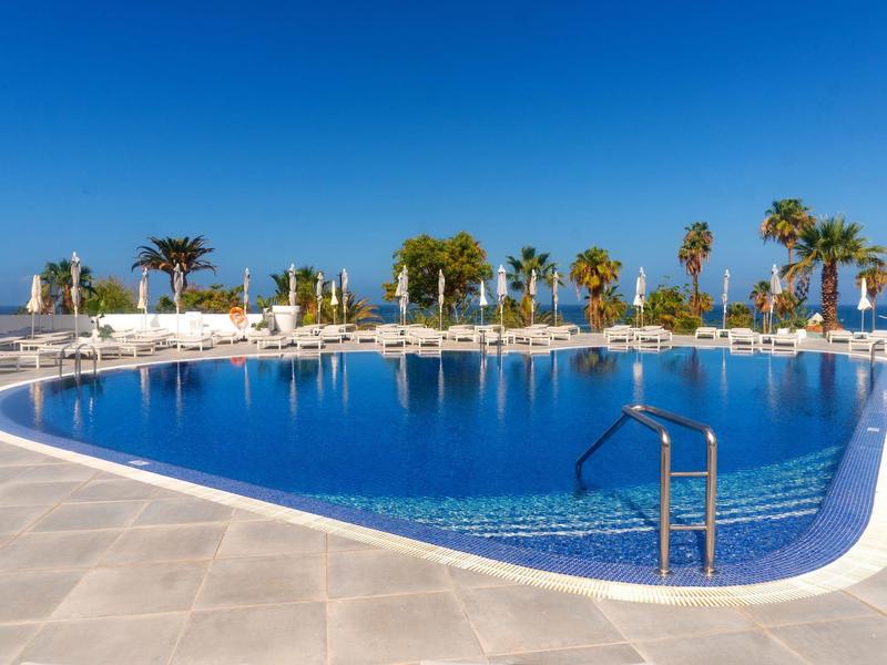 Großer Pool mit Palmen und Sonnenliegen unter klarem blauem Himmel