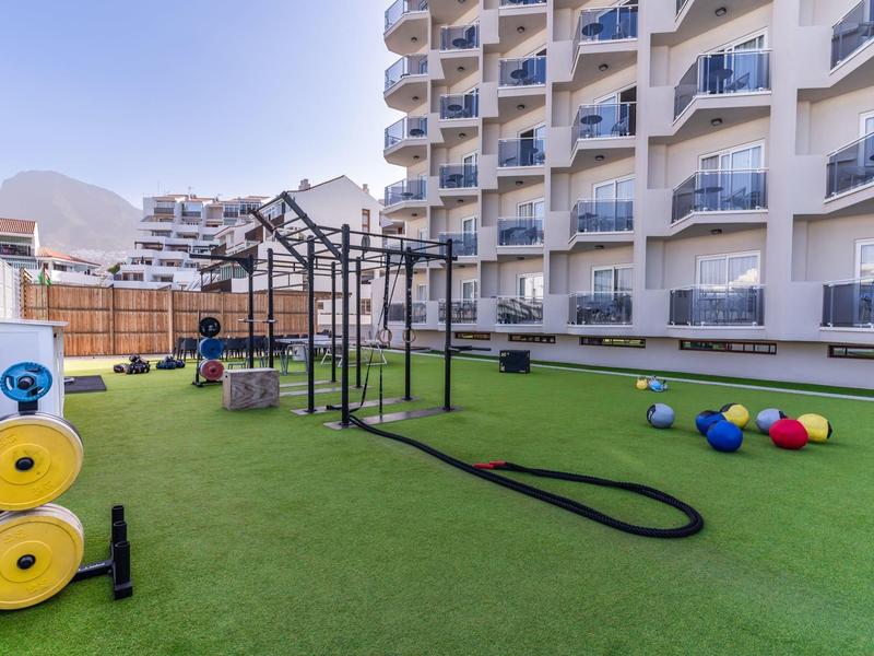 Außen-Fitnessbereich eines Hotels mit Klettergerüst, Gewichtsscheiben und bunten Bällen auf grünem Kunstrasen.