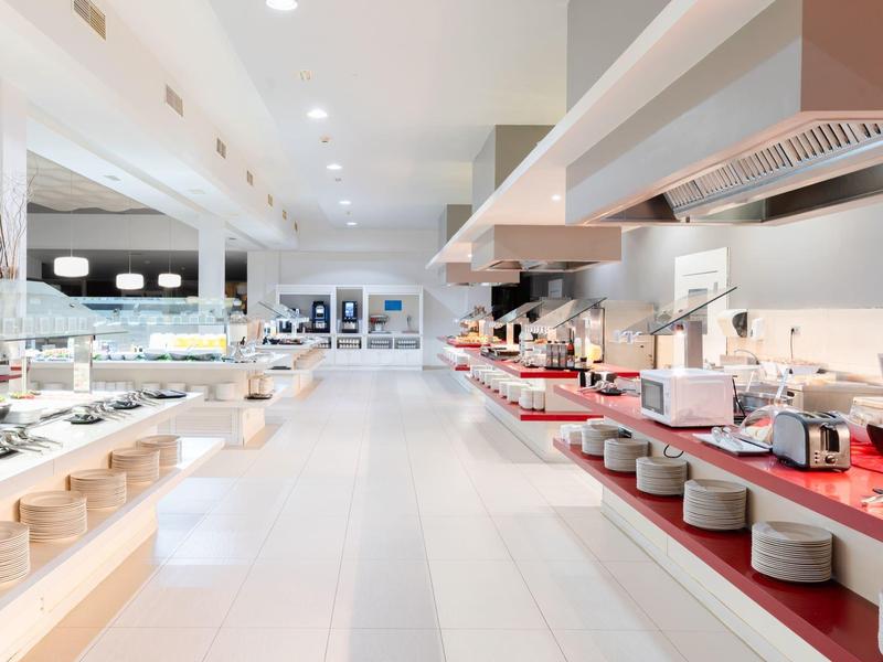 Helle, moderne Hotelküche mit langen Theken und offenen Regalen voller Teller und Küchenutensilien.