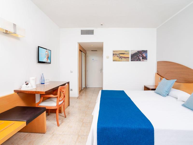 Helles Hotelzimmer mit zwei Betten, blauem Bettläufer und Schreibtisch mit Fernseher