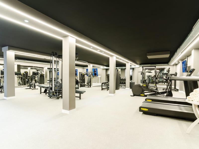 Moderner Fitnessraum mit Laufbändern und Trainingsgeräten in hellen Tönen.