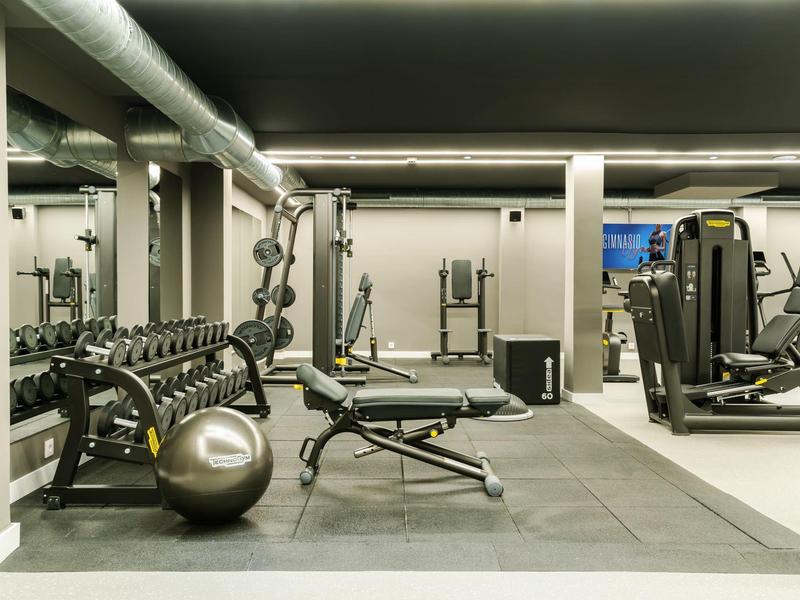 Moderner Fitnessraum mit Hanteln, Trainingsbank und Kardiogeräten in einem Hotel.