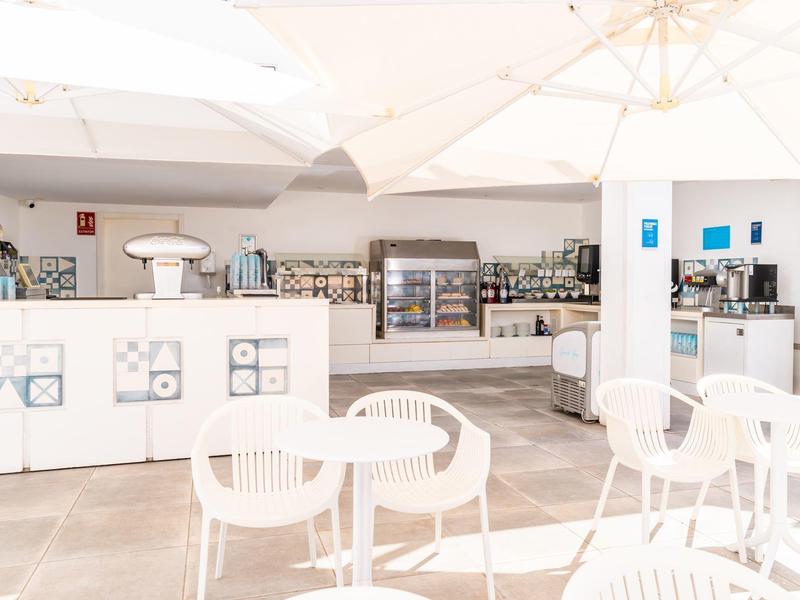 Helle, moderne Hotelbar mit weißen Tischen, Stühlen und großem Sonnenschirm.