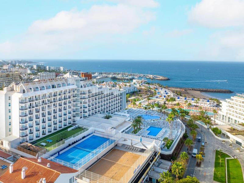 Großes Hotel mit Außenpool und Meerblick an der Küste unter blauem Himmel.