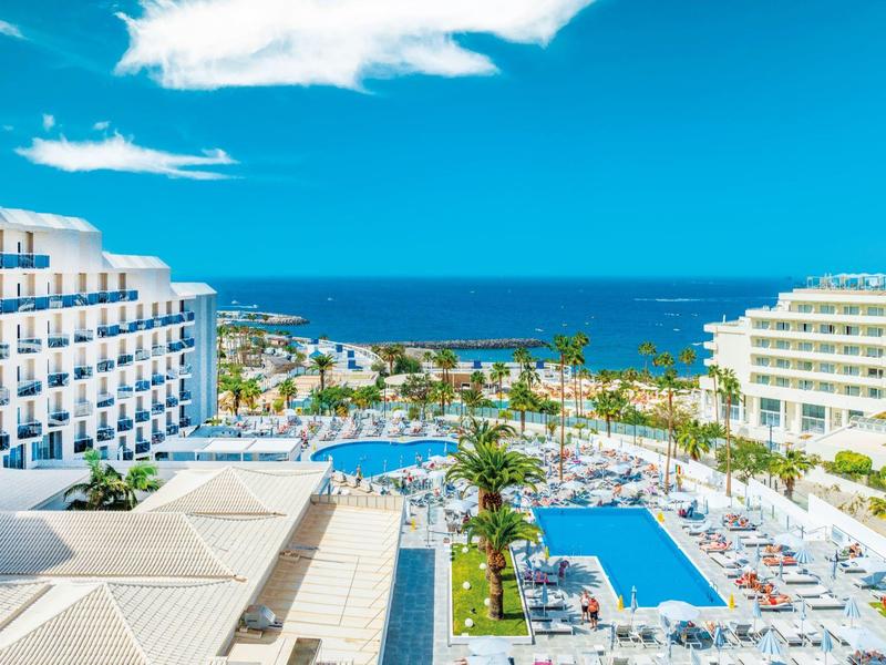 Hotelanlage mit Pools, Palmen und Blick auf das blaue Meer unter klarem Himmel.