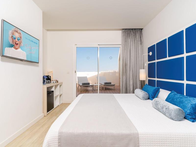 Modernes Hotelzimmer mit großem Bett, blauen Wandpaneelen und Balkon mit Meerblick.