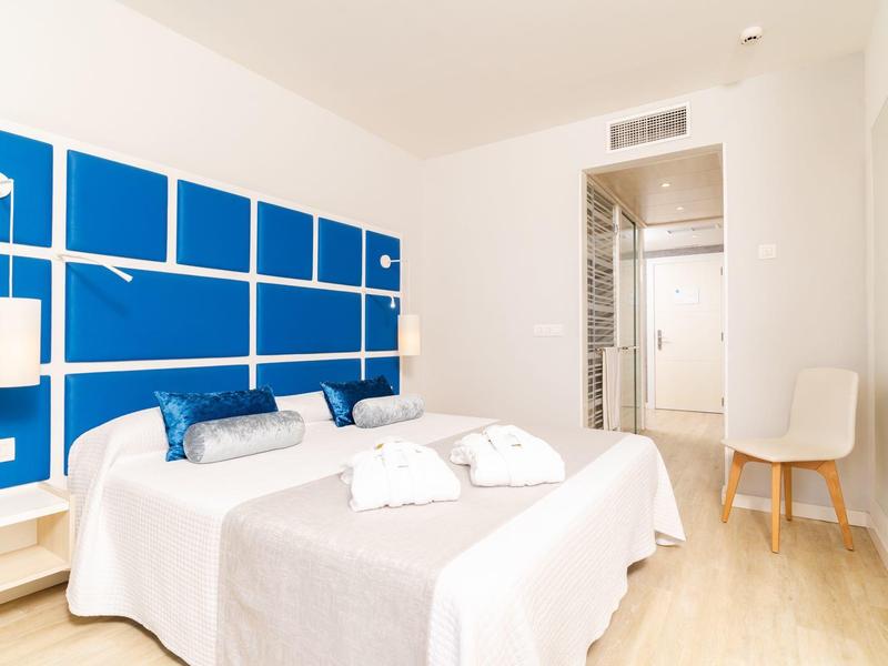 Modernes Hotelzimmer mit weißem Bett, blauen Kissen und großem blauem Wandpaneel.