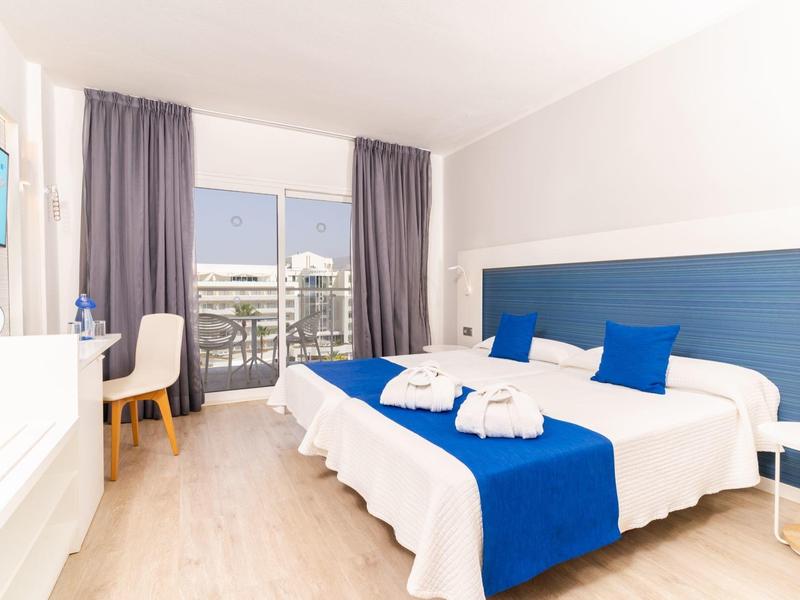 Modernes Hotelzimmer mit großem Bett, blauen Akzenten und Balkon mit Stadtblick.