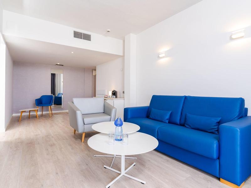 Helles Wohnzimmer mit blauem Sofa, grauem Sessel und zwei runden Tischen auf Holzfußboden.