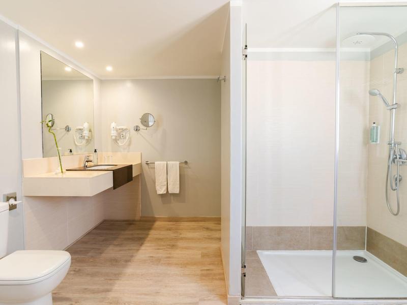 Helles Badezimmer mit Doppelwaschbecken, Toilette und Dusche mit Glastür.