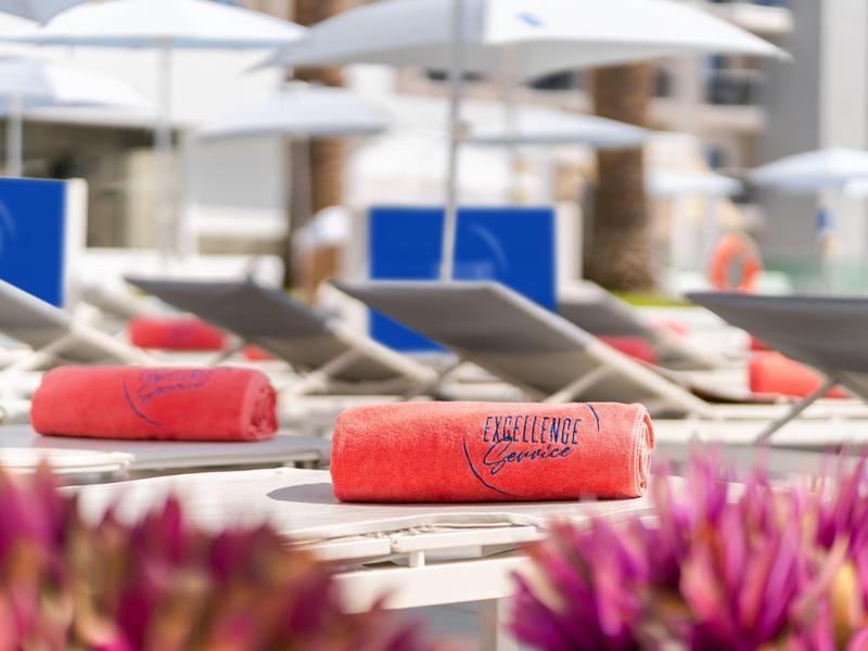 Rote Handtücher auf Liegestühlen neben Pool mit weißen Sonnenschirmen.